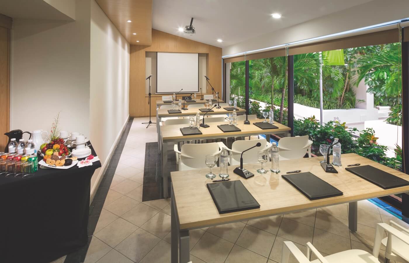 Sala de negocios pequeña para reunión con sillas frente a pantalla para proyectar con mesa de bocadillos y bebidas para descanso de café